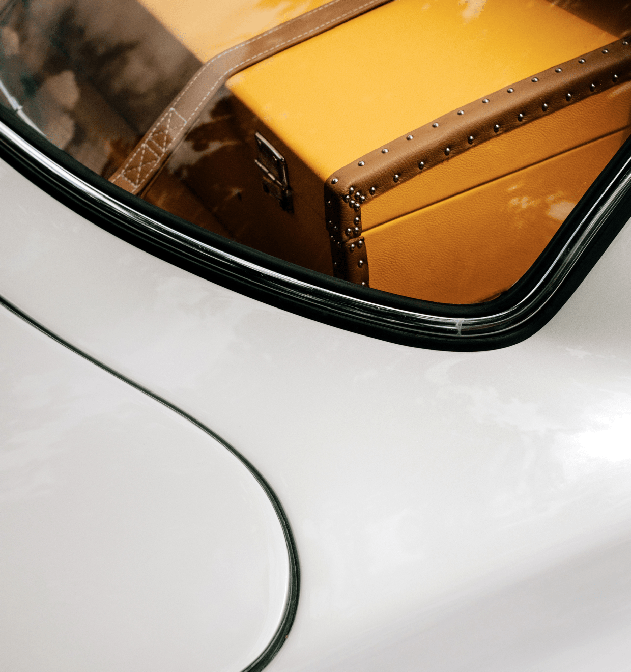 The back of a fancy white sports car showing a yellow retro suitcase Promo photo of a fancy white car