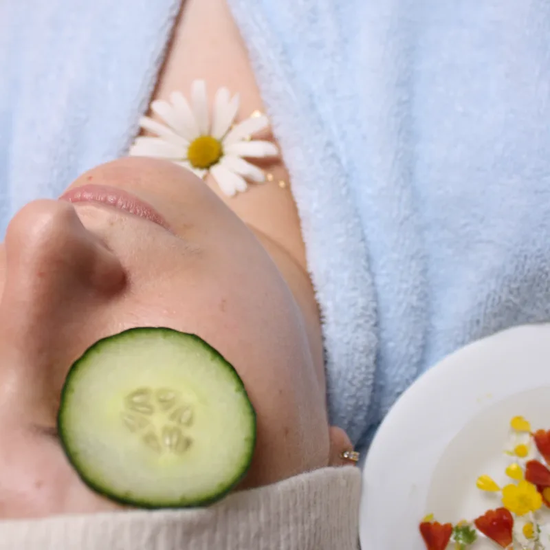 Woman in bathrobe lying down for wellness treatment with cucumbers on her eyes