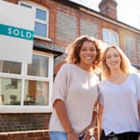 Two women next to sold sign Thumb
