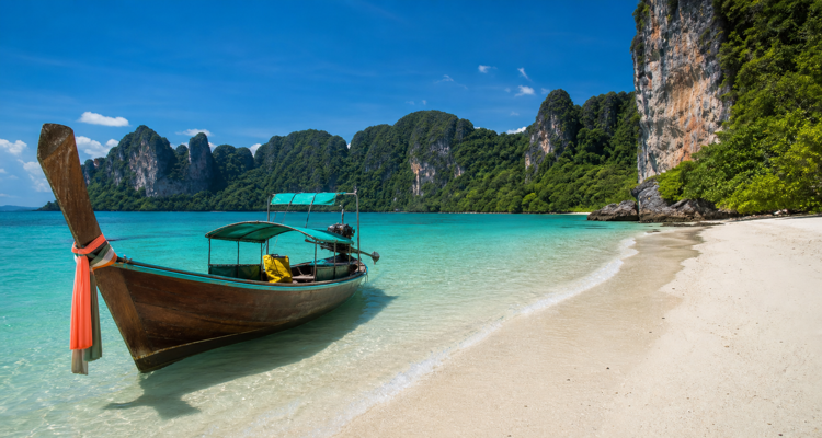 wooden-boat-on-tropical-beach-beneath-limestone-cliffs-750x400