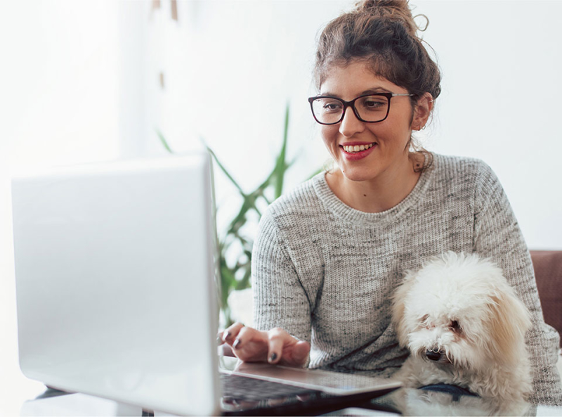 Woman with white poodle sitting at a laptop