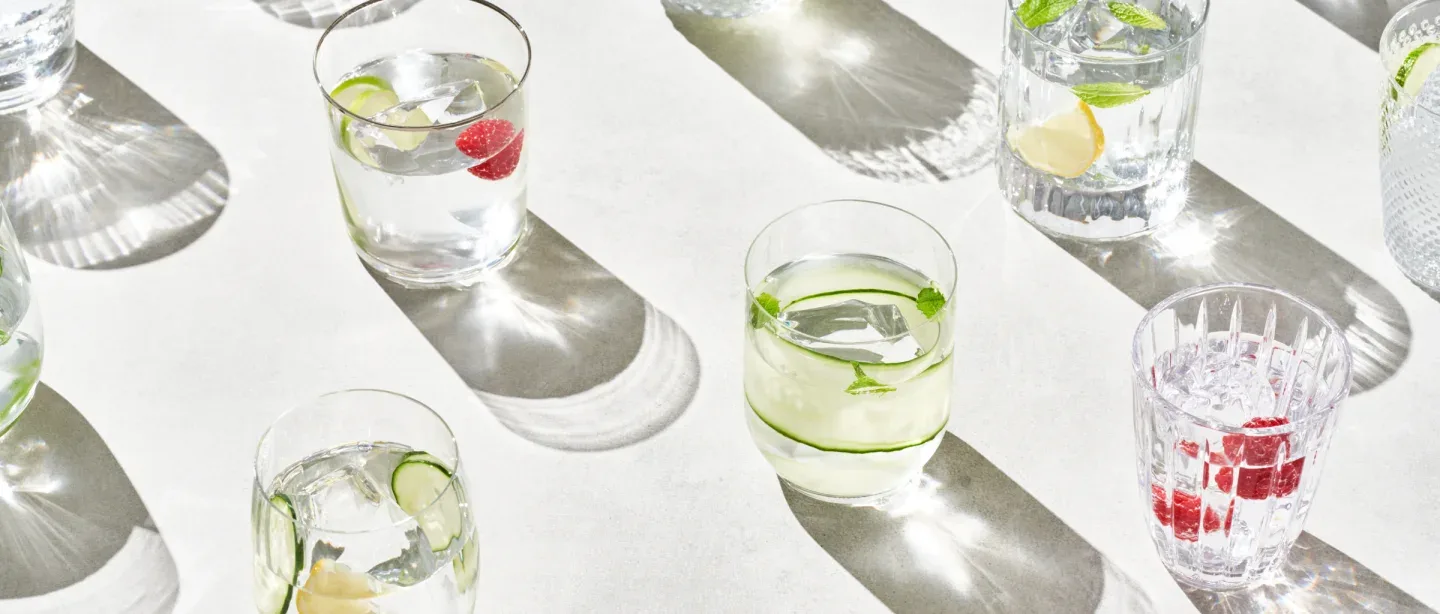 Several glasses of water with lemon, lime, and/or raspberries in them.