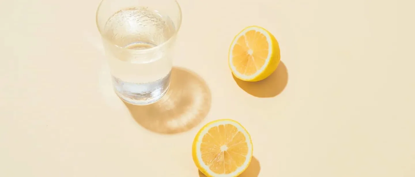Glass of water next to 2 lemon halves.