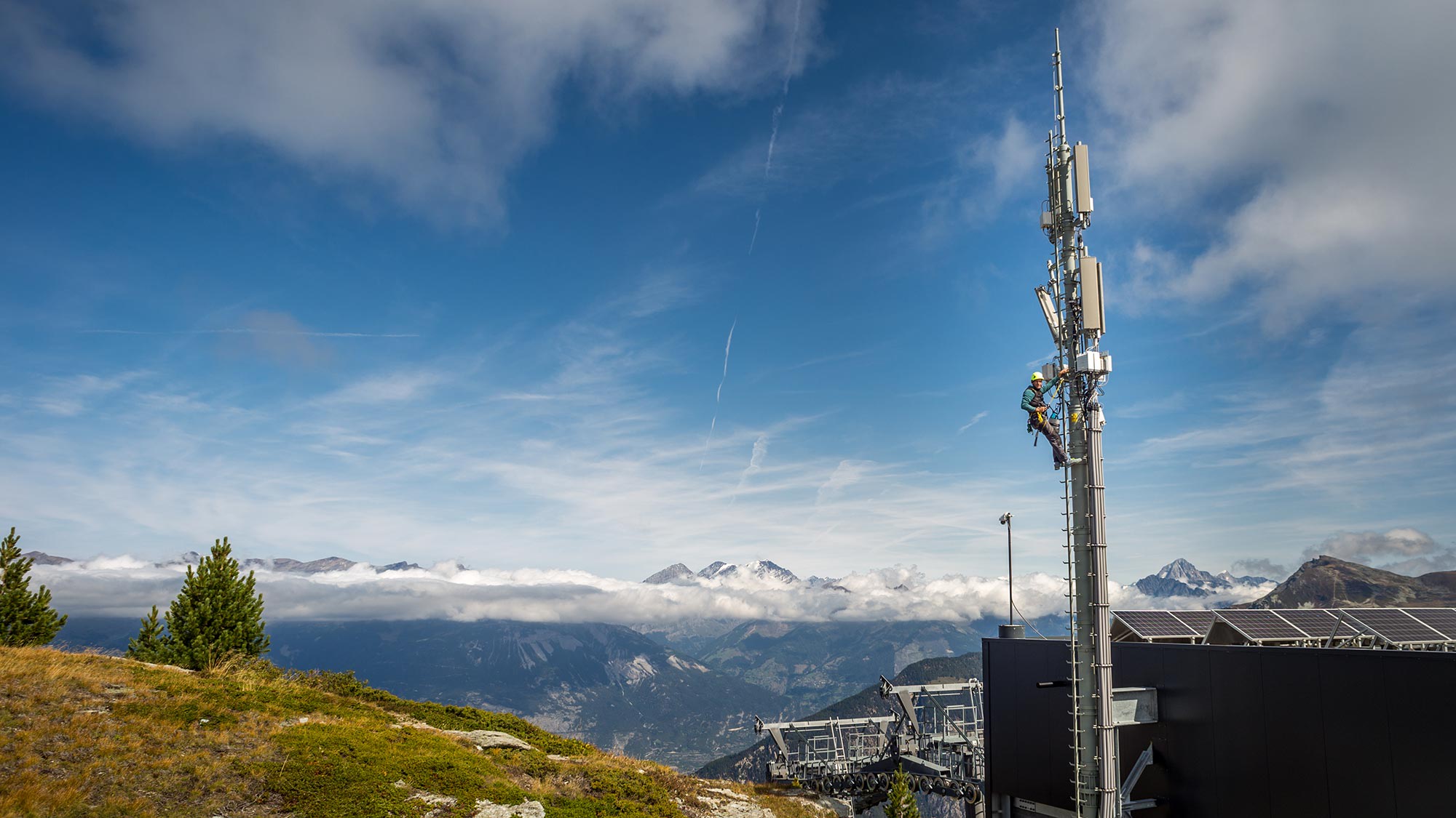 Mobilfunkmast ragt vor Bergkulisse in den blauen Himmel. Welche Bedingungen von Politik und Behörden geschaffen wurden und wie Betreiber das 5G-Netz aufbauen, erfahren Sie hier.