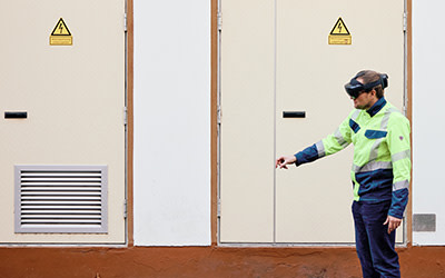 Ein Mann hat eine Virtual-Reality-Brille an und steht mit ausgestreckter Hand vor einem Stromkasten. 
