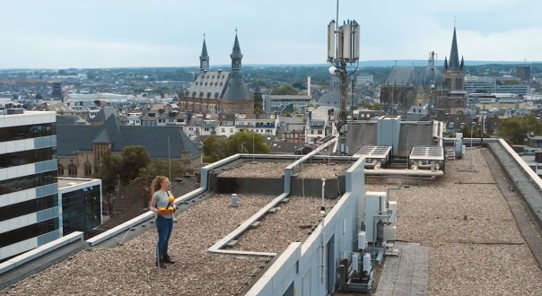 Wissenschaftliche Arbeiterin steht mit einem Funkmessgerät auf einem Dach. 