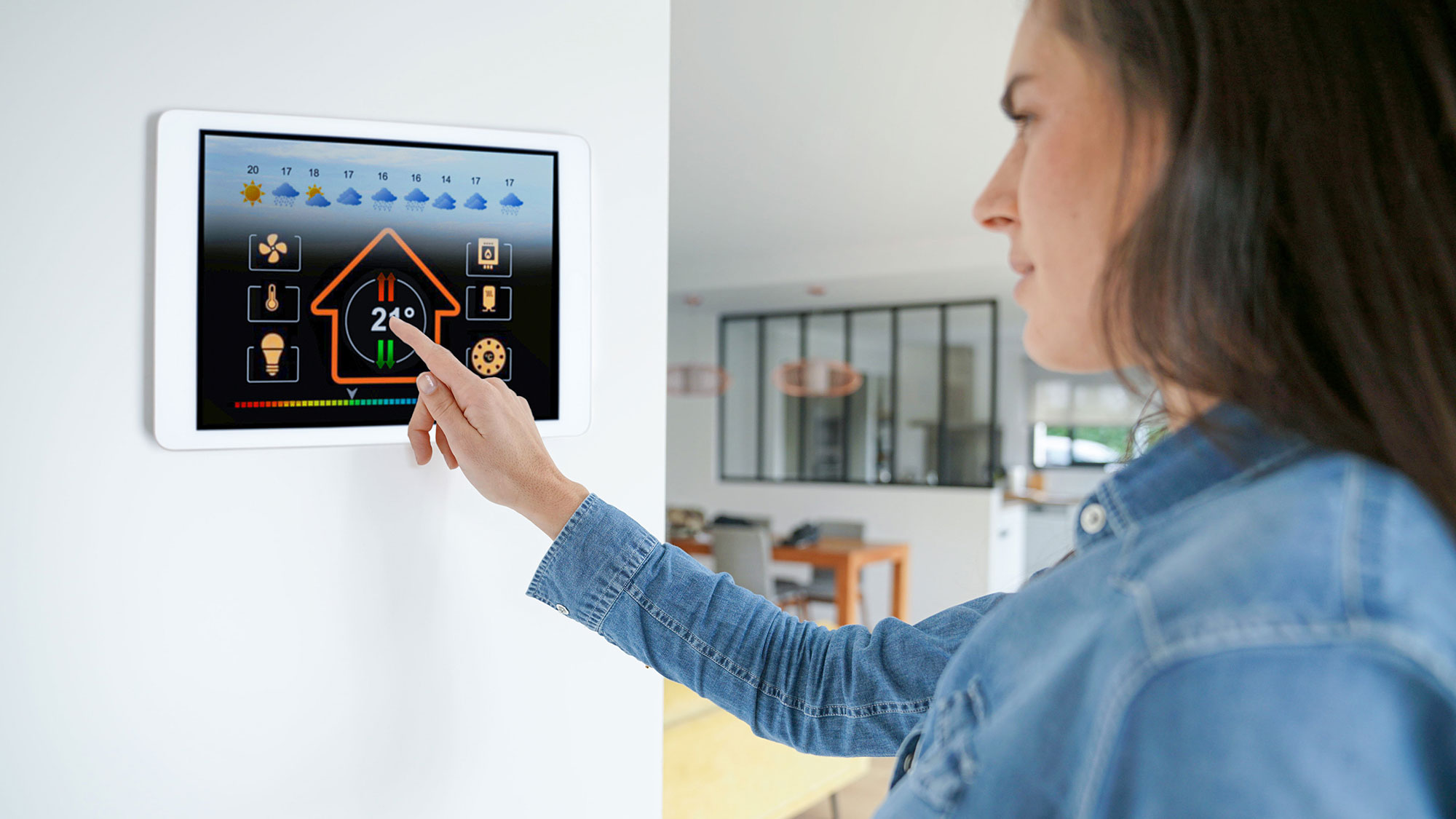 Eine Frau in Jeanshemd bedient ein Smart Home System auf dem Tablet an der Wand. Das neue 5G-Netz birgt neun Vorteile für unseren Alltag.