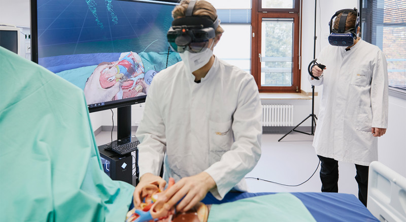 Bastian Dewitz (rechts) spielt den implantierenden Arzt. Er sieht in seiner Brille das Bild, das auch auf dem großen Monitor gezeigt wird. Dieses Bild nimmt Roman Bibo just in diesem Moment während der Explantation (vorne links) auf.