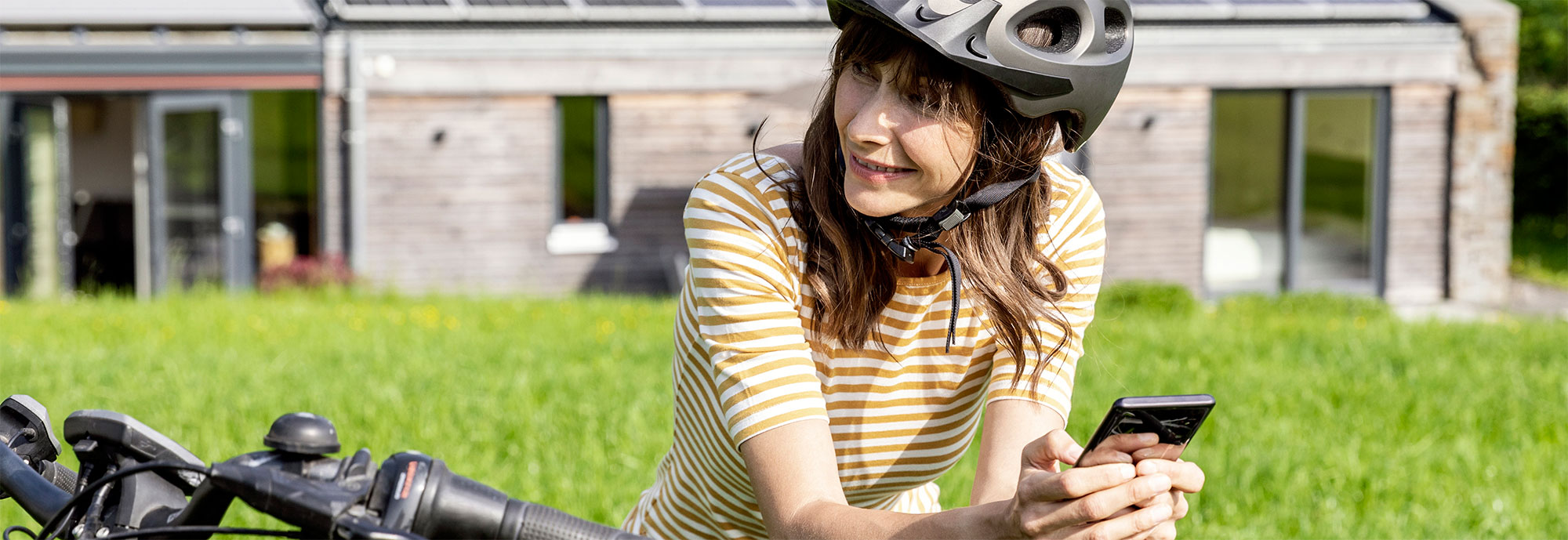 Radfahrerin steht vor grüner Wiese und hält ihr Smartphone in den Händen. 
