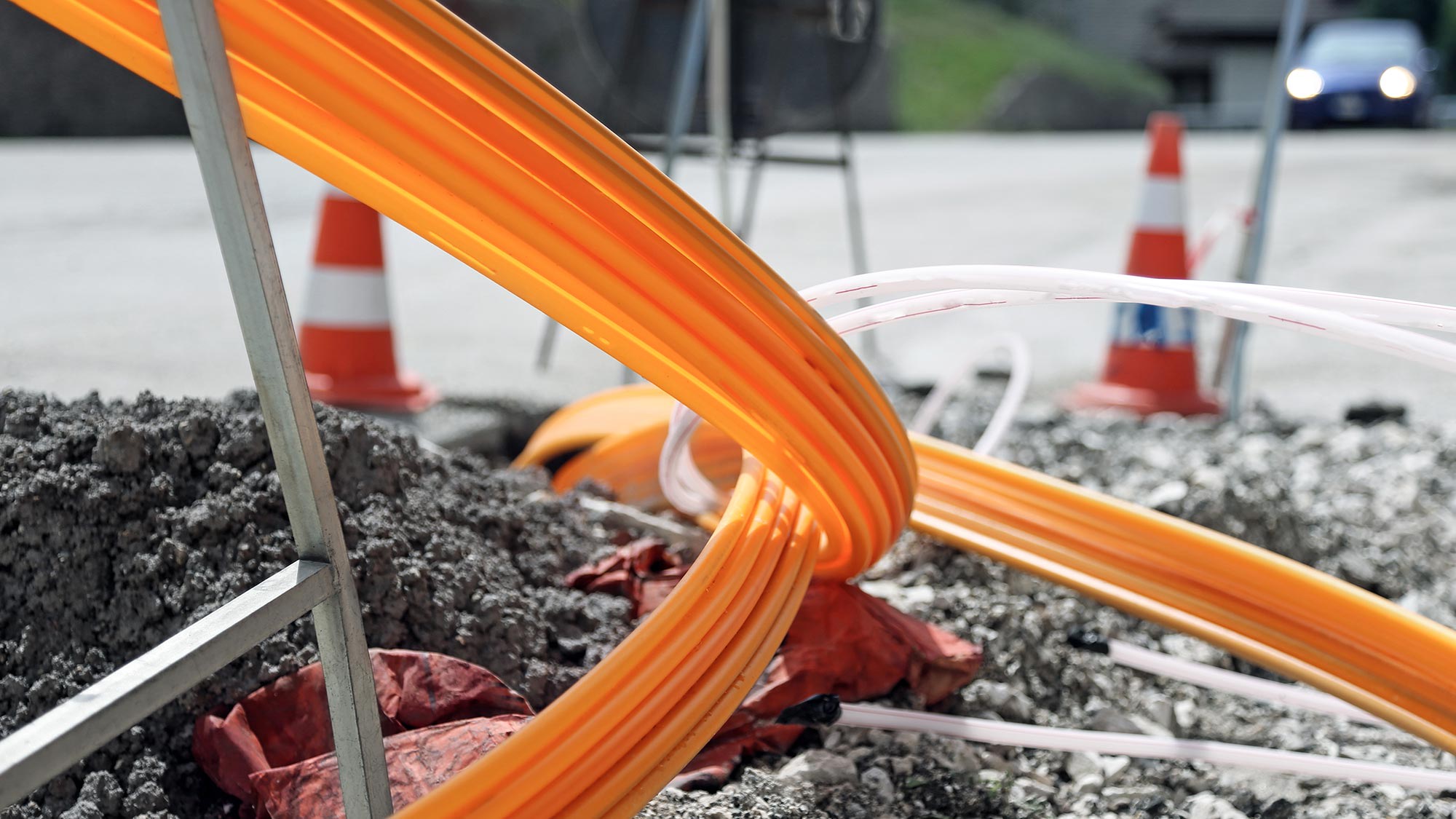 Glasfaserkabel ragen aus Baustelle auf einer Straße. Glasfaserleitungen sind die beste Möglichkeit, um das 5G-Netz zum Sendemast zu bringen. 
