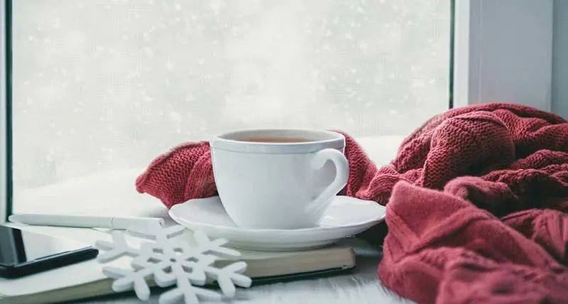A cup of coffee in front of a window with a wintry backdrop.