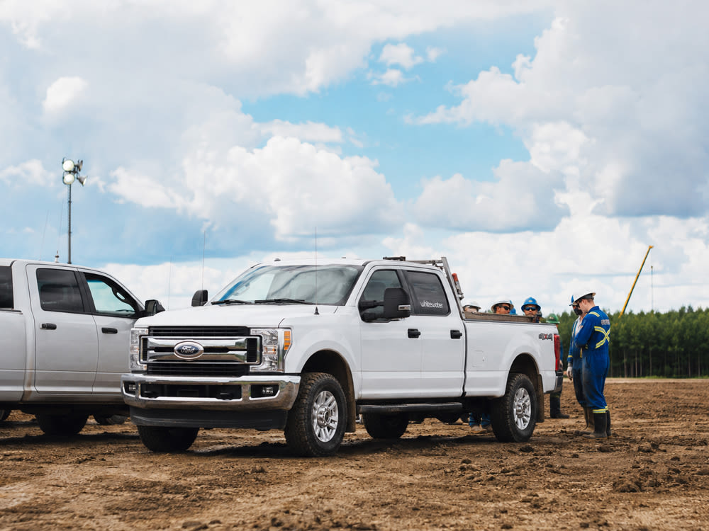 2 camions Ford blancs dans un champ avec des travailleurs en uniformes et casques de chantier pour Whitewater Management LP