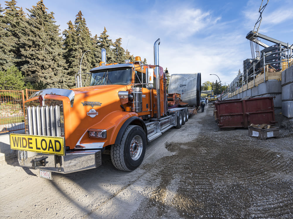 Orange truck with a "wide load" placard on the grill, stationed at a worksite