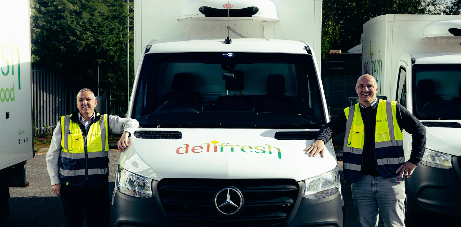 Deux employés en gilets jaunes de sécurité posant devant un camion de livraison blanc Mercedes-Benz de l'entreprise Delifresh.