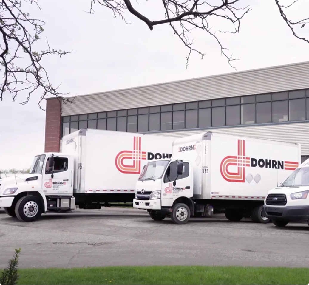 Two white Dohrn delivery trucks and a van parked outside a commercial building on an overcast day.