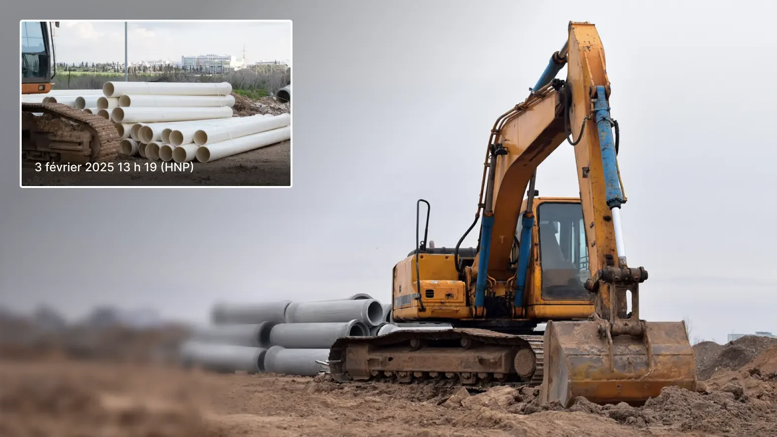 Une pelleteuse jaune sur un chantier de construction avec des piles de tuyaux en béton