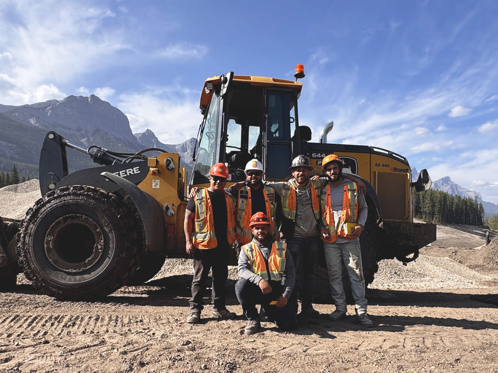 Construction workers standing beside a John Deere tracking smiling under a blue sky