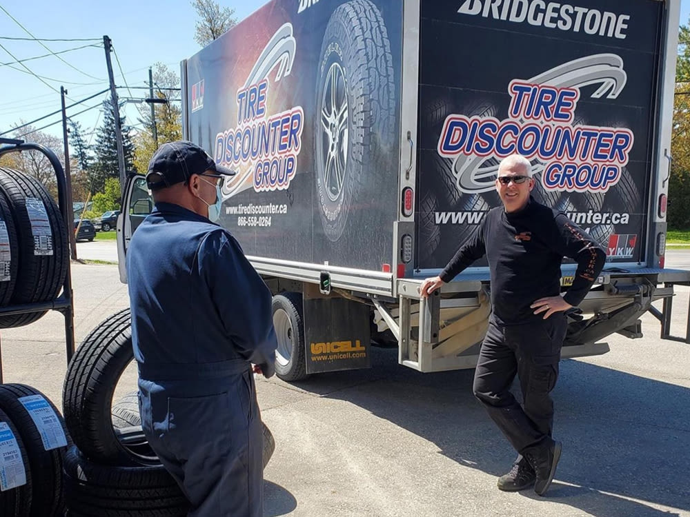 Homme en chemise noire à manches longues devant un camion de Tire Discounter Group avec un homme en combinaison bleue.