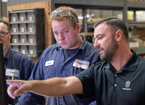 Three men around a computer; one is pointing at the screen while explaining what they are looking at