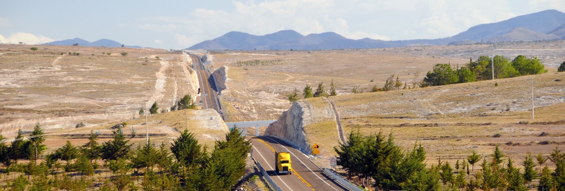 Yellow trucks drives along freeway next to grassy hills