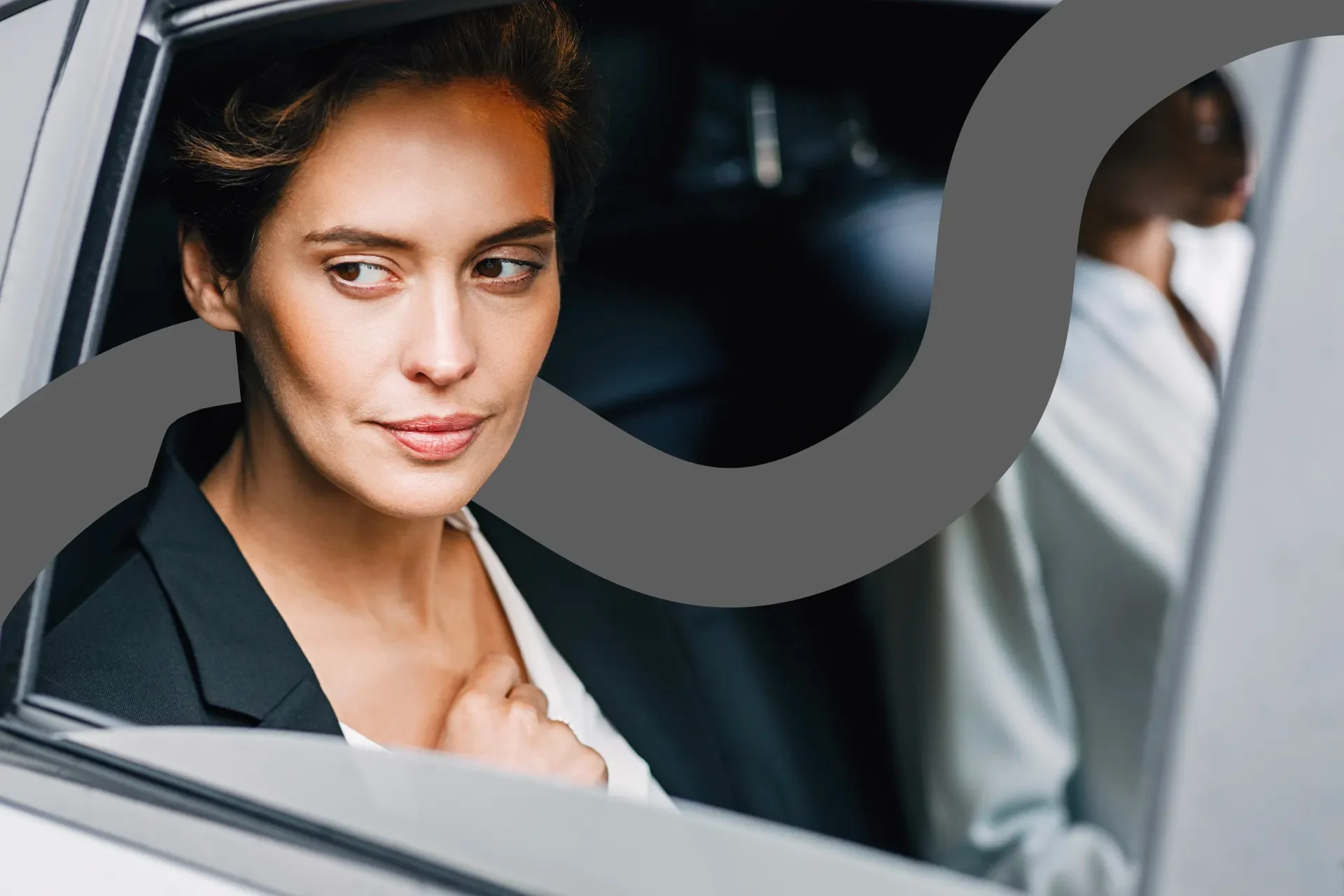 A professional woman in a dark blazer gazes out of a car window with a confident, thoughtful expression.