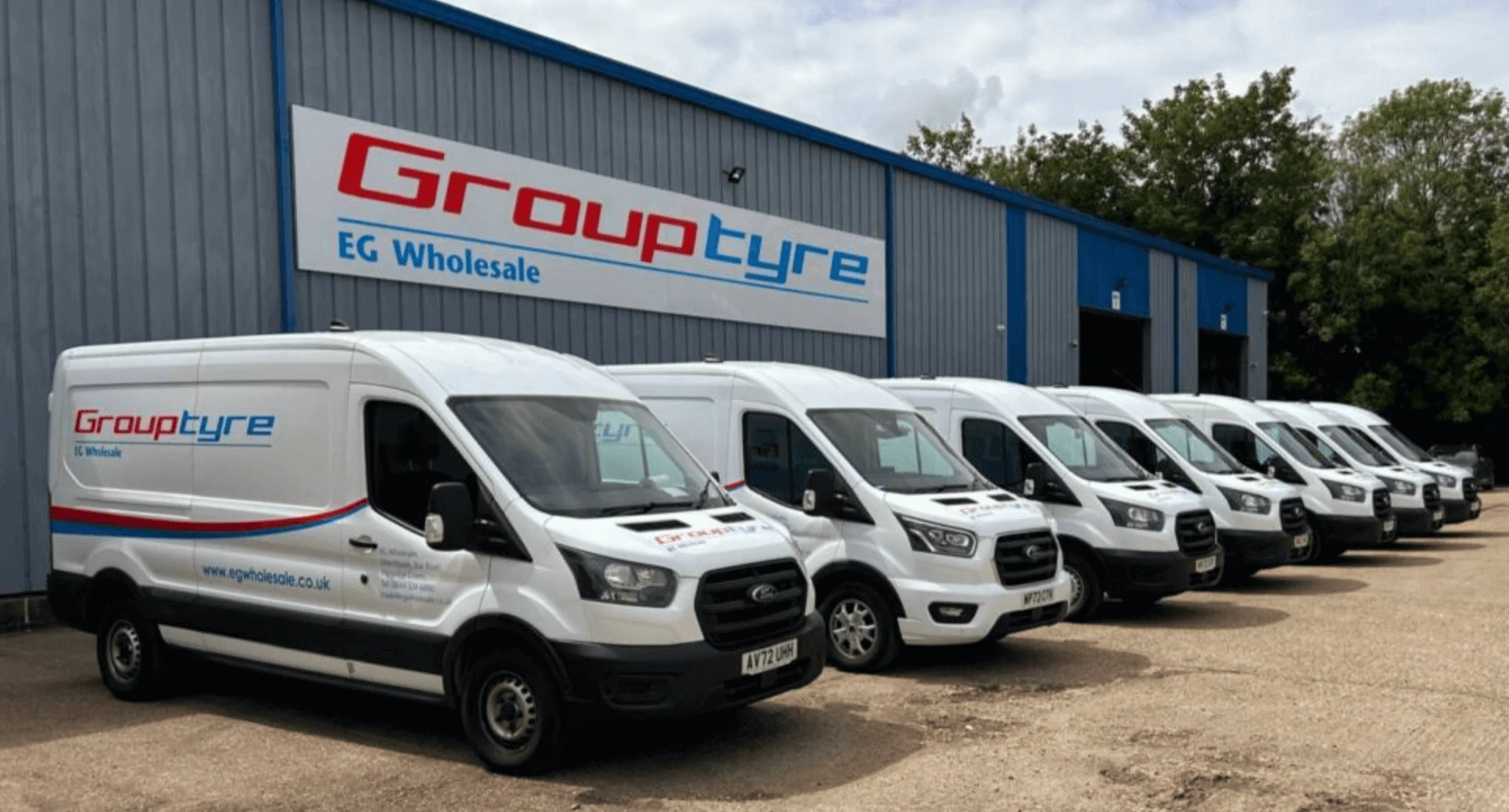 Reihe weißer Lieferwagen vor dem Grouptyre EG Wholesale Gebäude mit blauer Fassade und Firmenlogo.