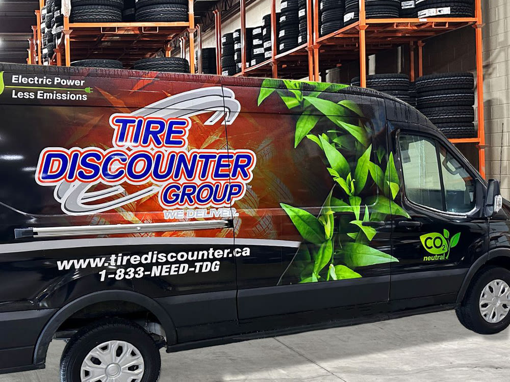 Camion de Tire Discounter Group dans un entrepôt avec des pneus noirs sur des étagères orange en arrière-plan.