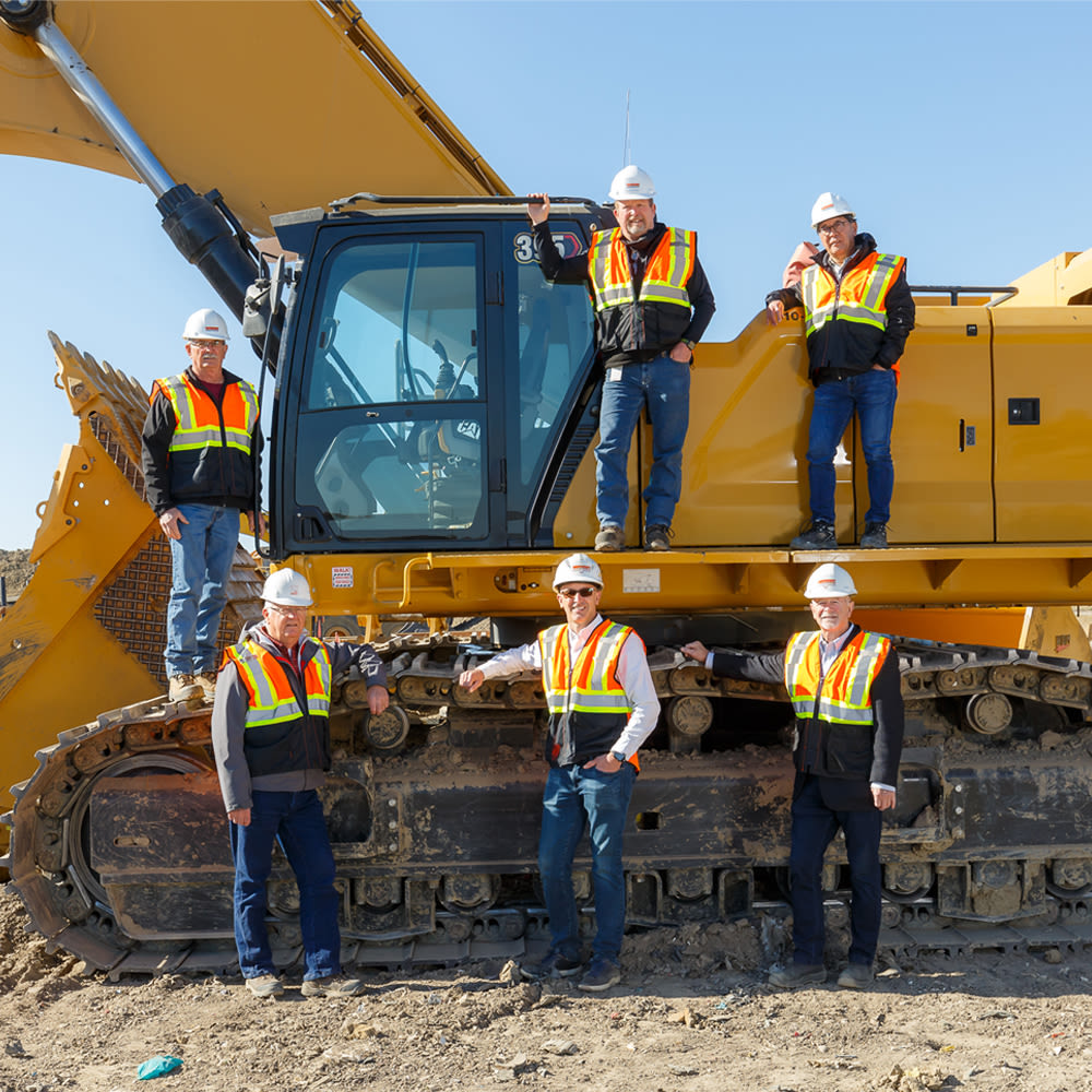 Workers in construction vests and hard hats standing beside a yellow CAT excavator