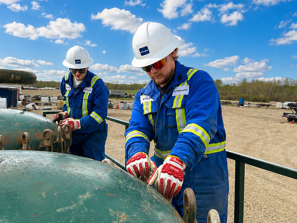 Two workers with hard hats and field working clothes change valves on a gas valve for Whitewater Management LP