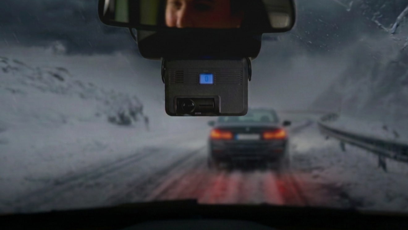 Dashcam fixée au rétroviseur d'une voiture roulant sur route enneigée, avec un véhicule devant aux feux rouges allumés.