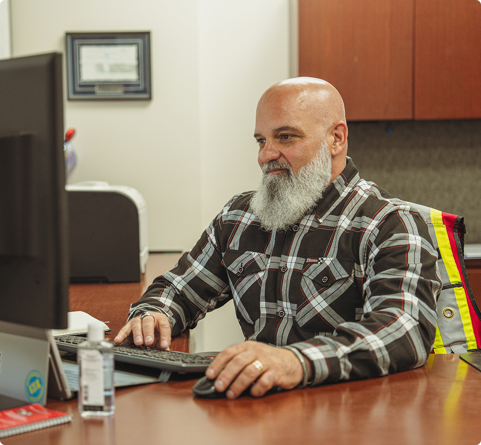 An operations manager sits in an office reviewing data on his computer.