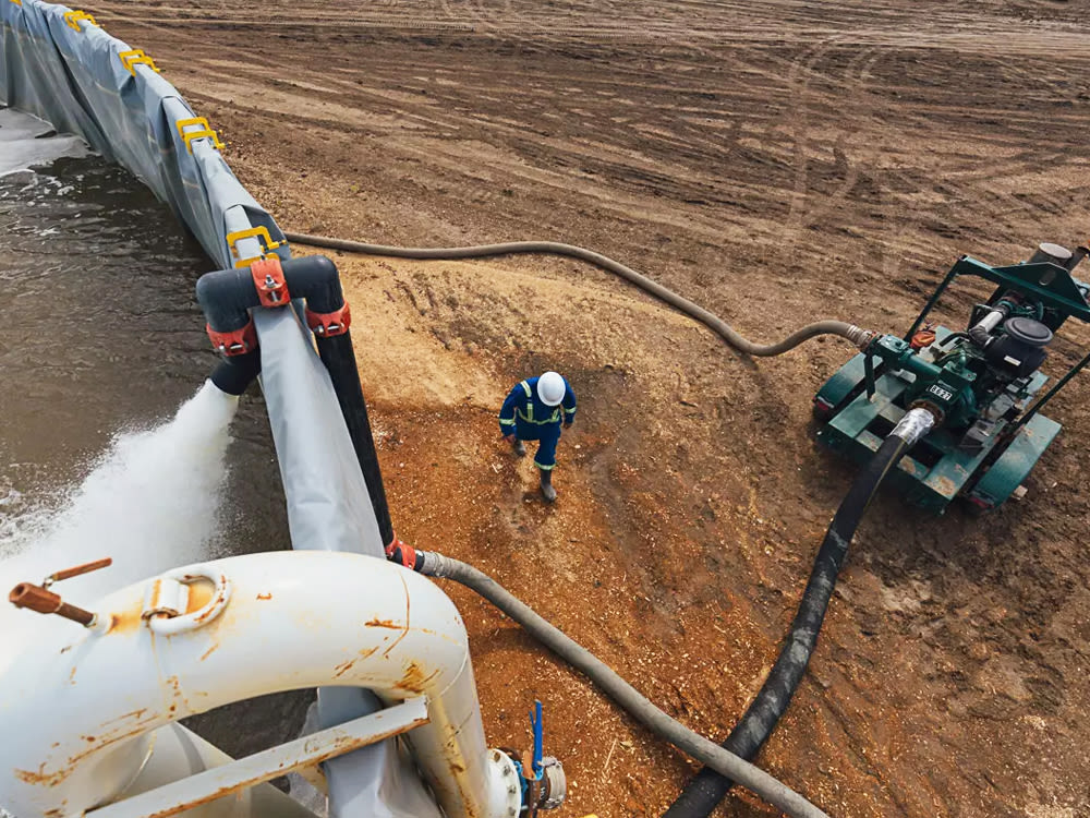 Worker wearing a hard hat walking on dirt site between a water pumping machine and a pool