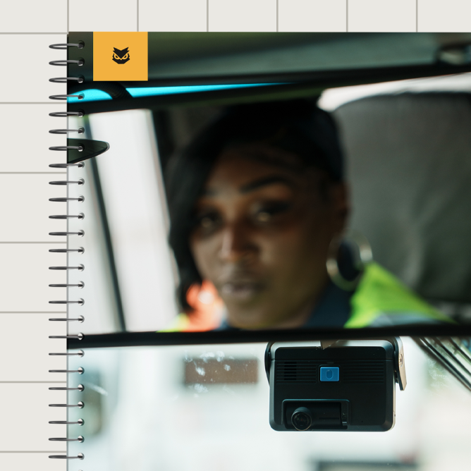 Driver reflected in rearview mirror wearing a cap and safety vest, with a dashcam mounted on the windshield.