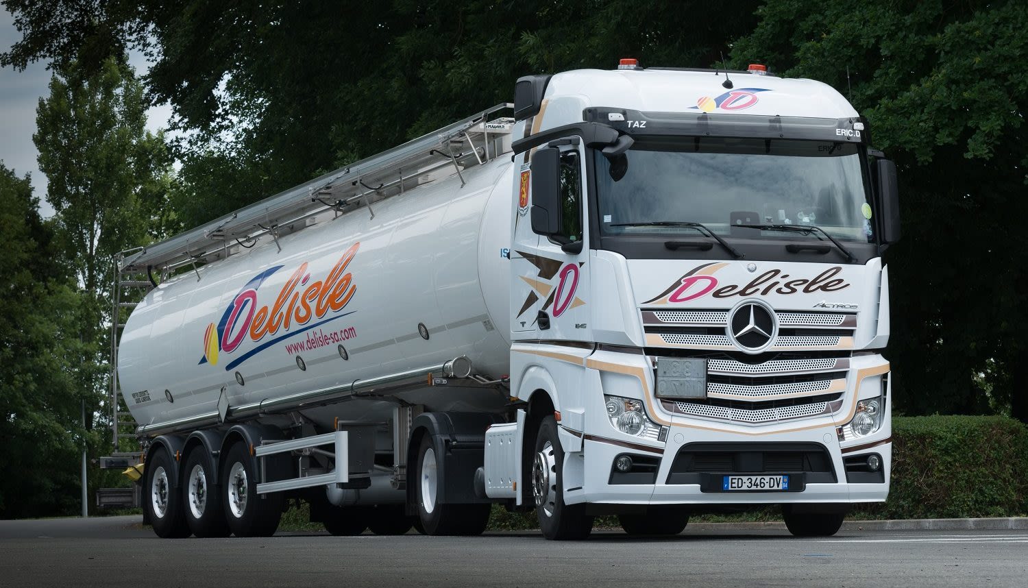 Camion-citerne blanc Mercedes-Benz Actros de la société Delisle sur une route, entouré d'arbres verts.