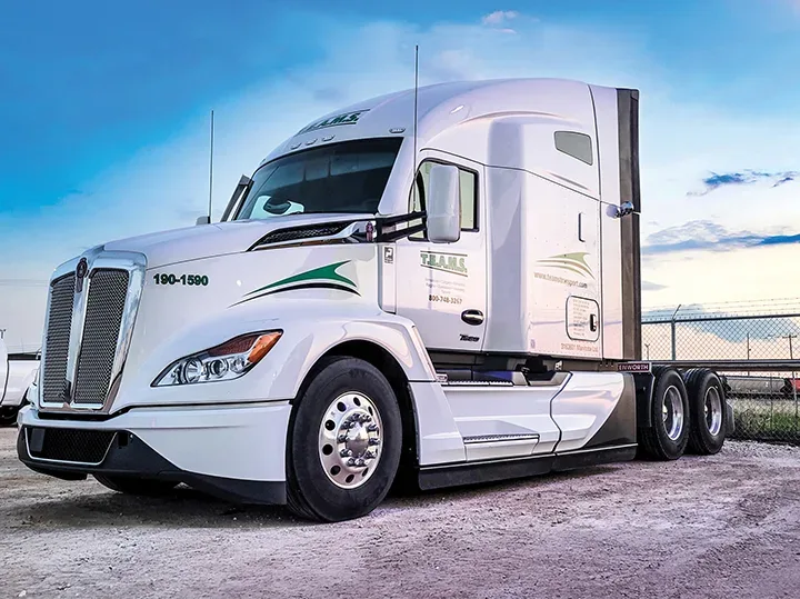 Camion semi-remorque blanc Kenworth avec accents verts, stationné sous un ciel bleu clair.