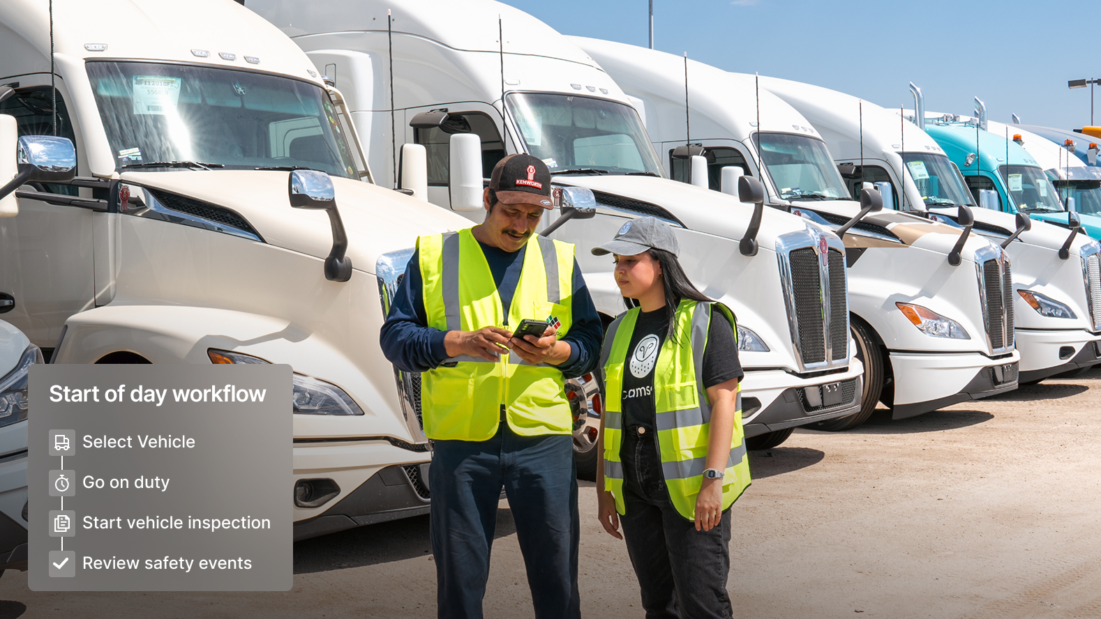 Two drivers looking at a phone in front of a truck fleet