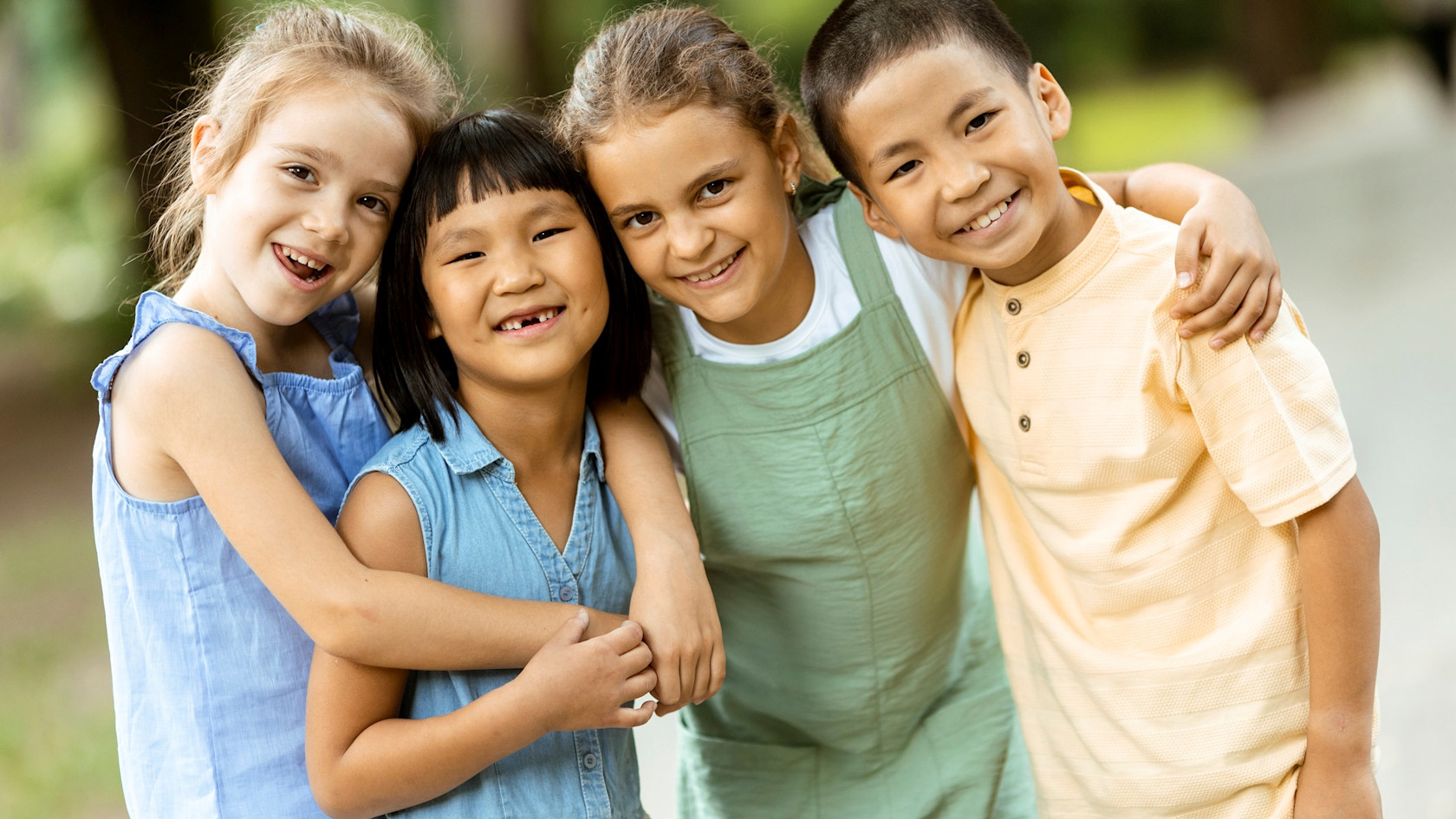 Four smiling and beaming children, three girls and a boy, all hugging each other.