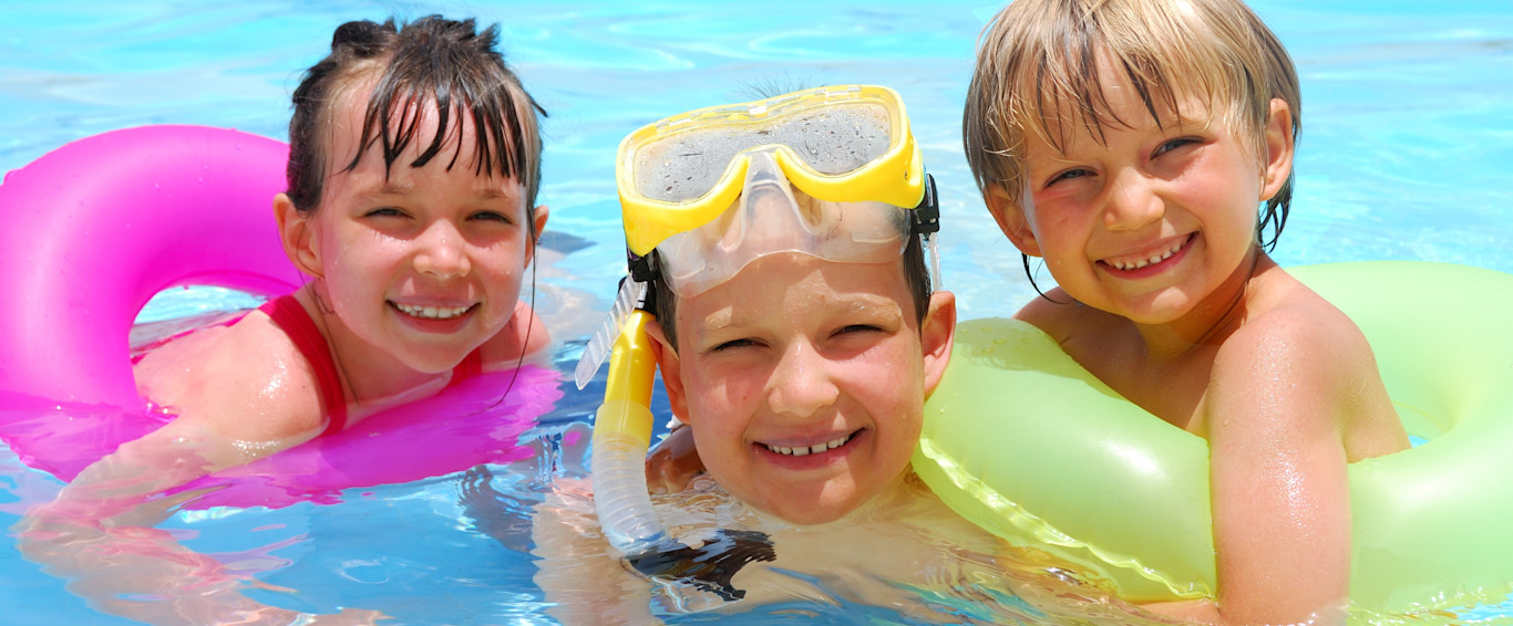 Three laughing children in the water with diving goggles and swimming tires.
