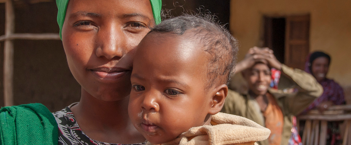 A mother holding a child in her arms, looking at the camera.