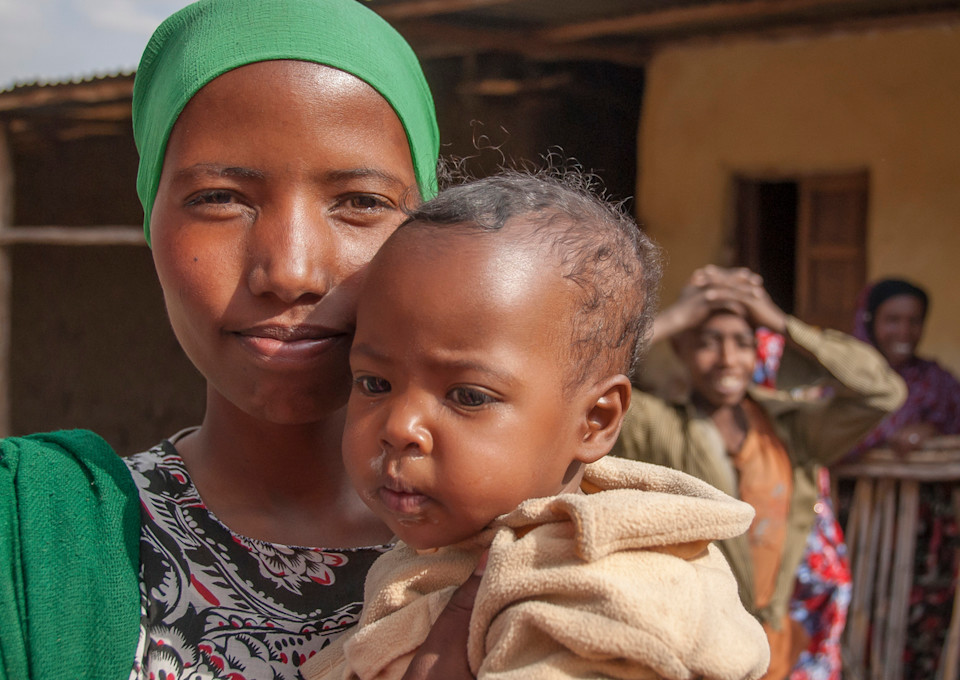 A mother holding a child in her arms, looking at the camera.