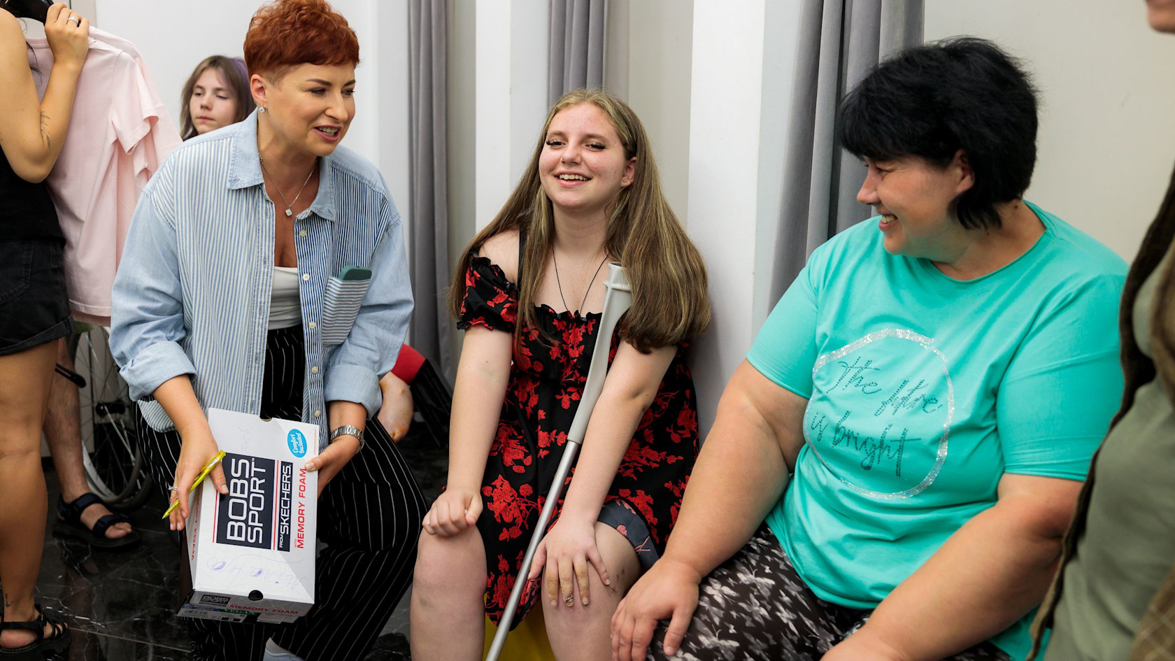 A Ukrainian girl with crutches, she has a war injury, together with SOS carers and parents choosing beautiful clothes.
