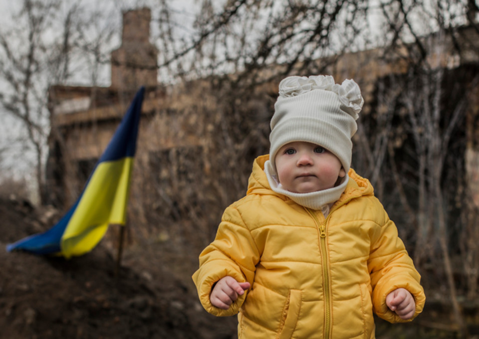 Little girl in front of defensive structures of Ukrainian army. War in Ukraine. Children and war concept. Support for Ukraine. Stop war. Humanitarian disaster concept. Ukrainian flag.