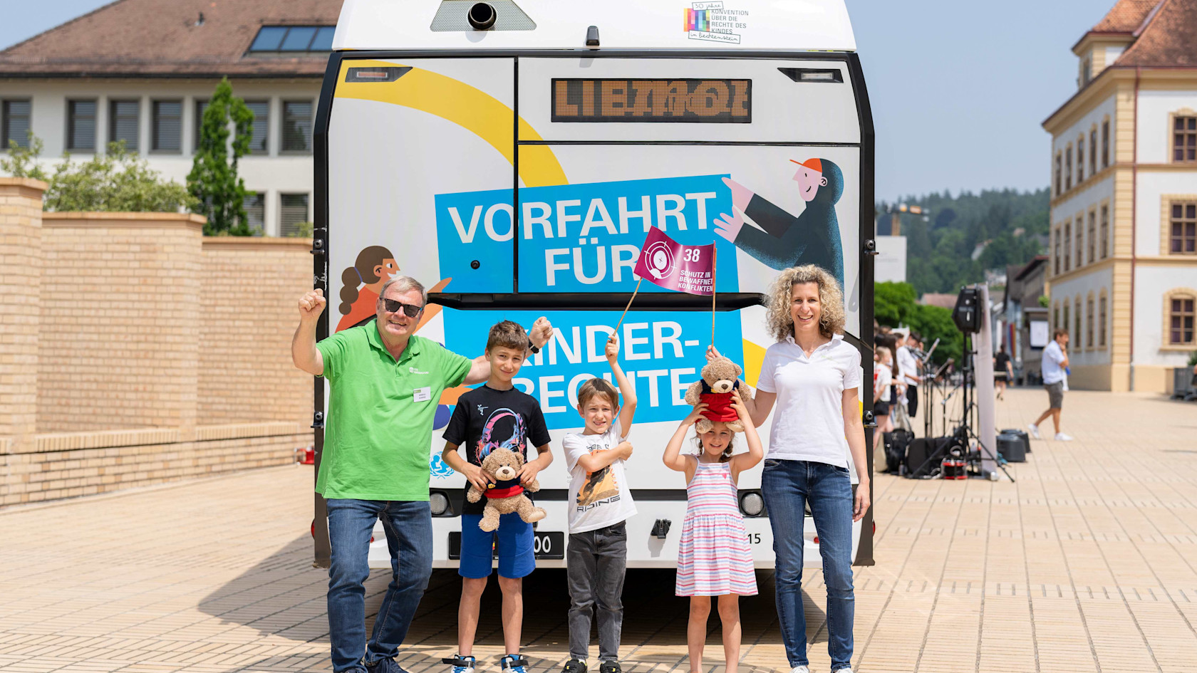 Markus von SOS-Kinderdorf sowie Maike mit ihren Kindern vor dem LieMobil Bus mit einer Fahne zu den Kinderrechten.