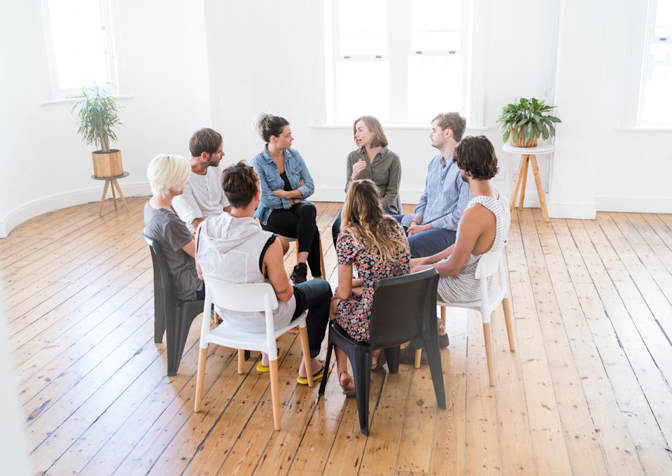 Mehrere Erwachsene sitzen während einer Gruppentherapie im Kreis und tauschen sich aus.