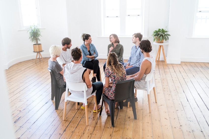 Several adults are sitting in a circle during a group therapy session, sharing their thoughts.