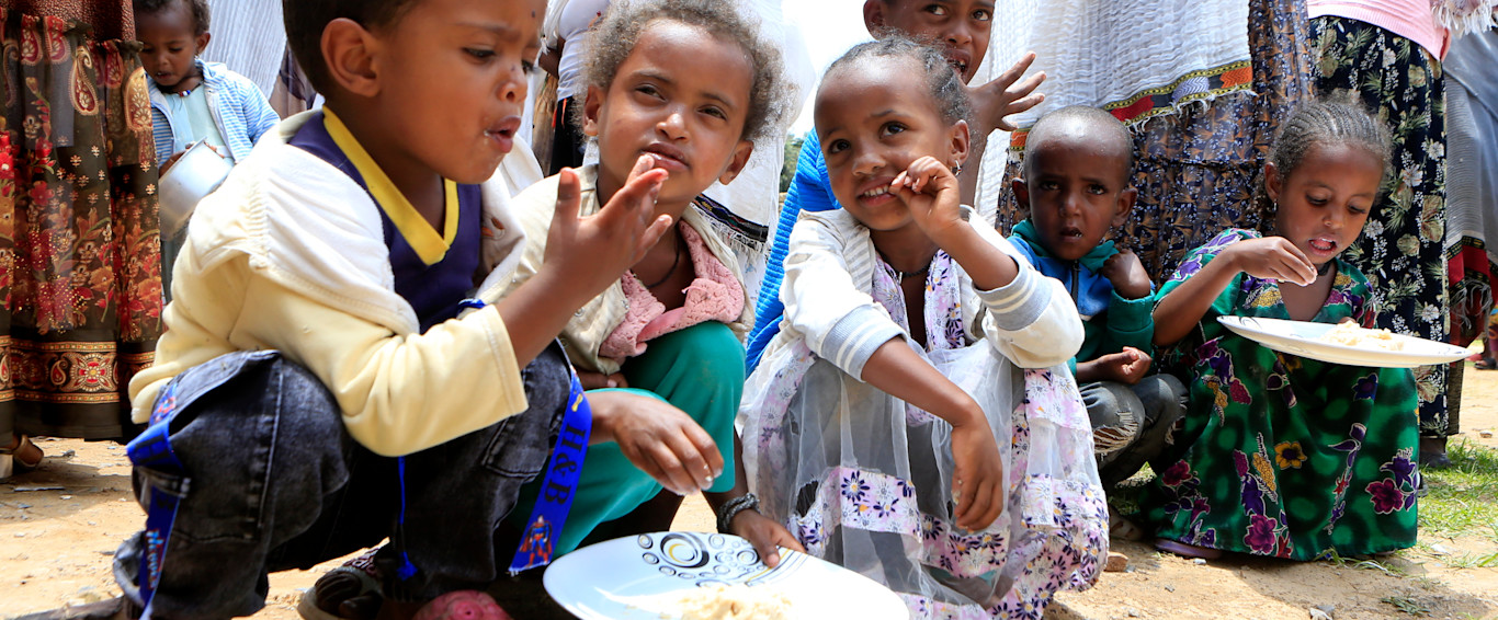 Three Ethiopian children sit on the floor and eat from a plate.