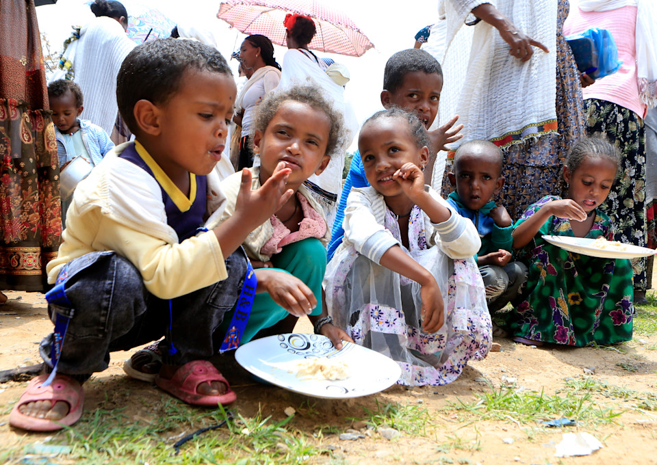 Three Ethiopian children sit on the floor and eat from a plate.