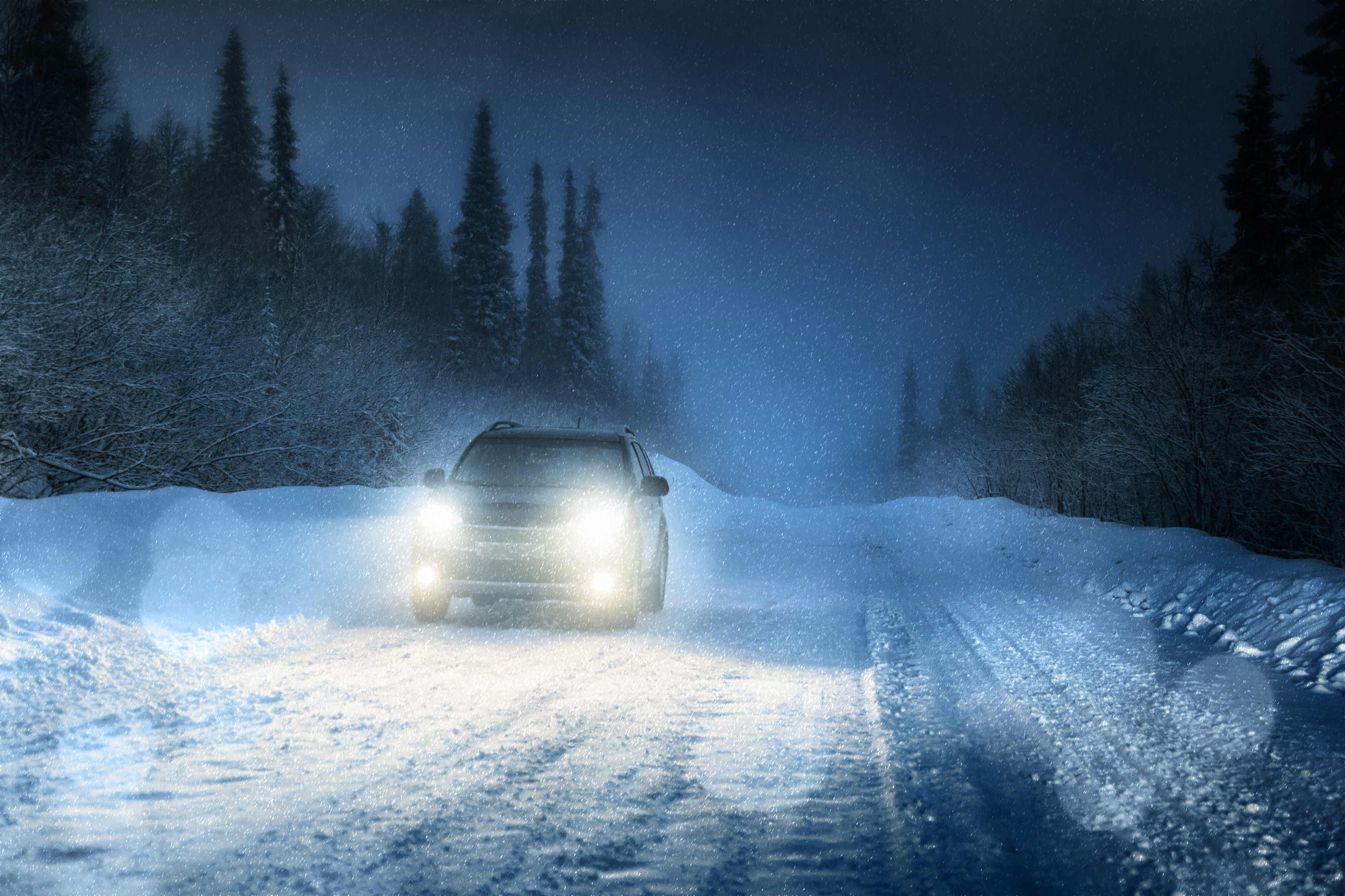 Car with headlights on driving down a winter road at night