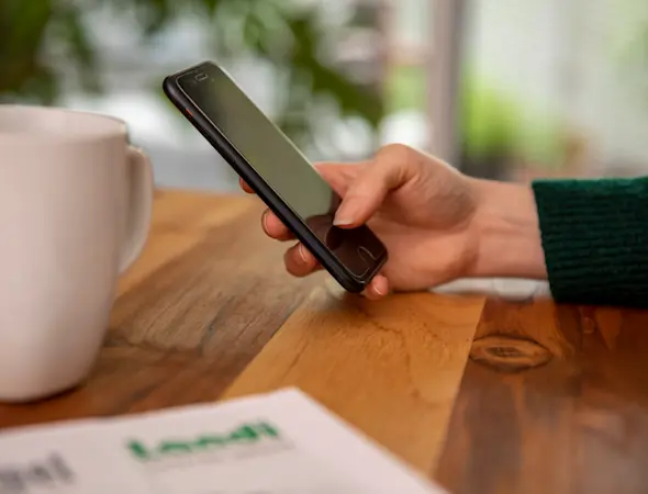 Hand mit Handy, Kaffeetasse und AGROaktuell angeschnitten auf Tisch