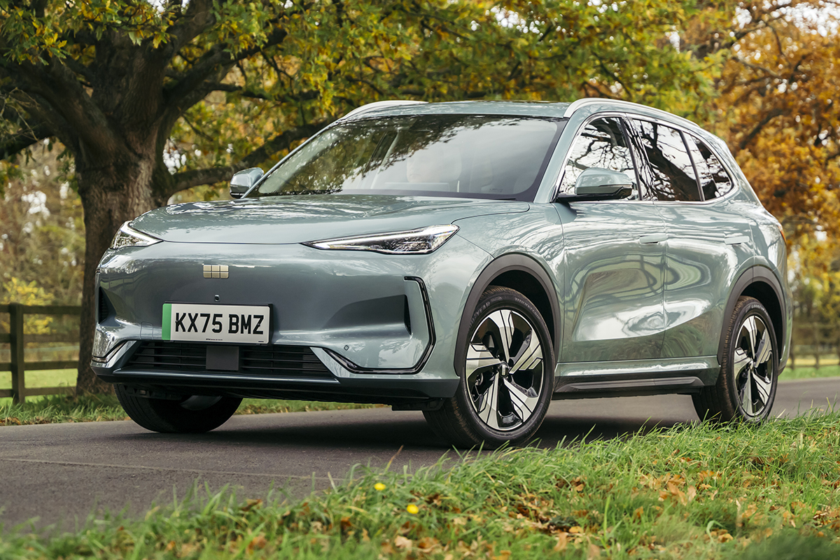 Geely EX5 parked on country road with autumn trees displaying orange and green foliage in background.